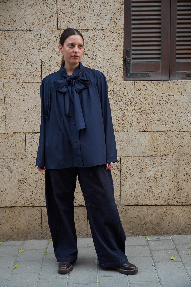 Model wearing a dark blue blouse with a large bow and dark blue jeans