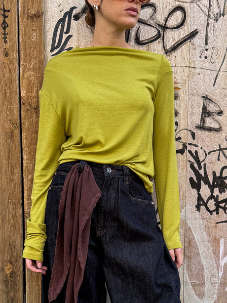Model wearing a green long-sleeve top and dark jeans