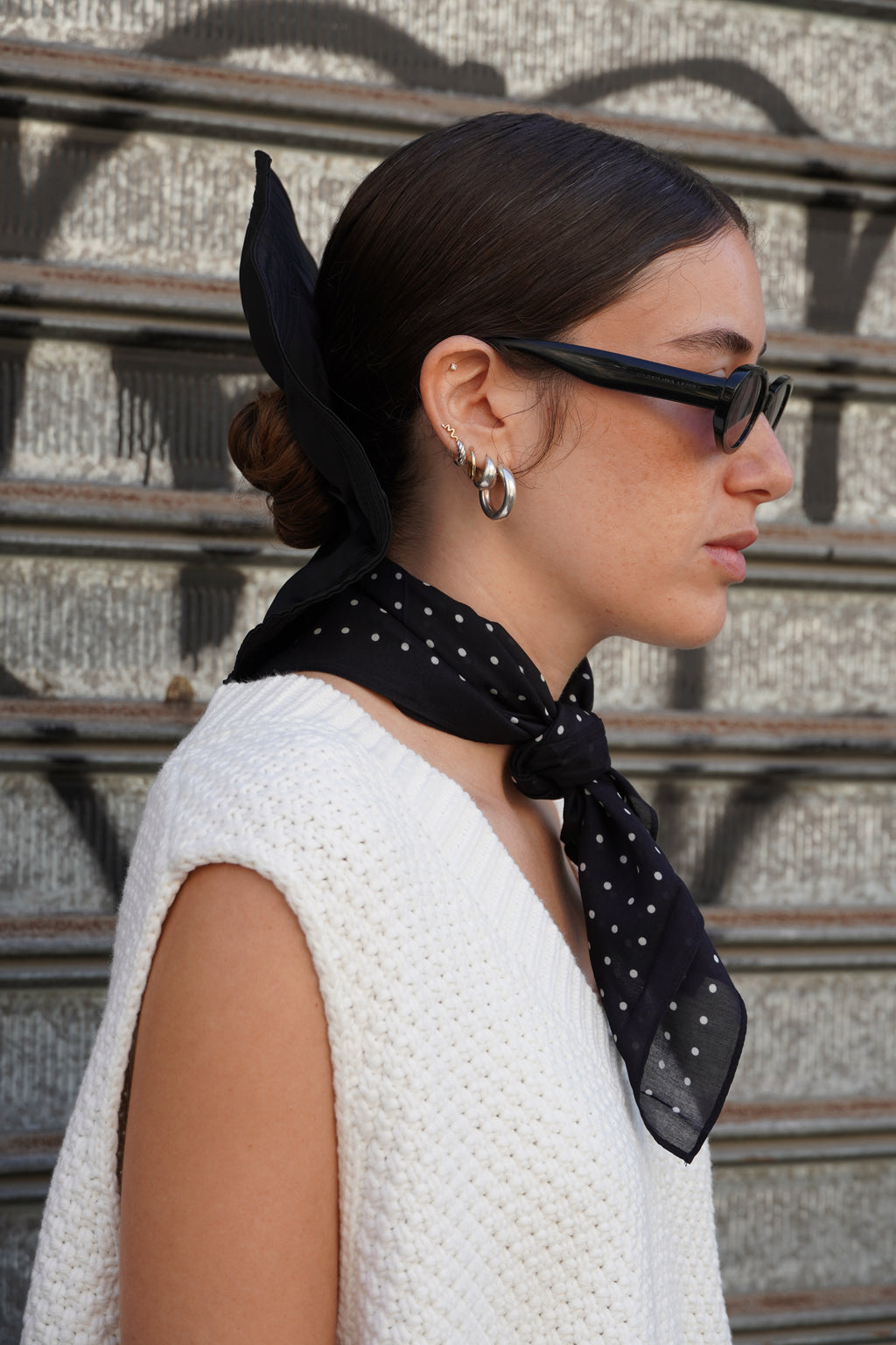 Model wearing a black polka dot scarf, with a white knitted vest