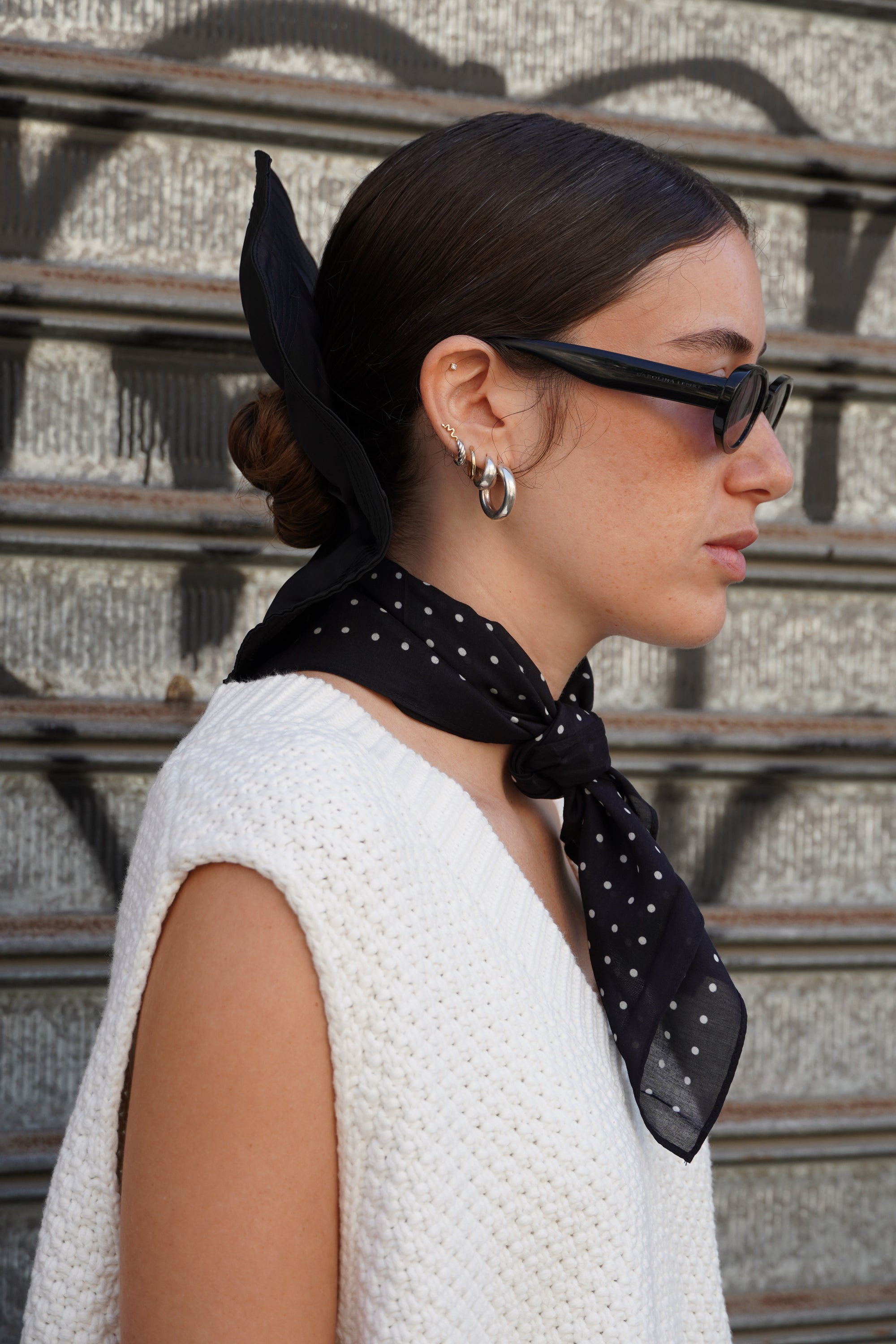 Model wearing a black polka dot scarf, with a white knitted vest