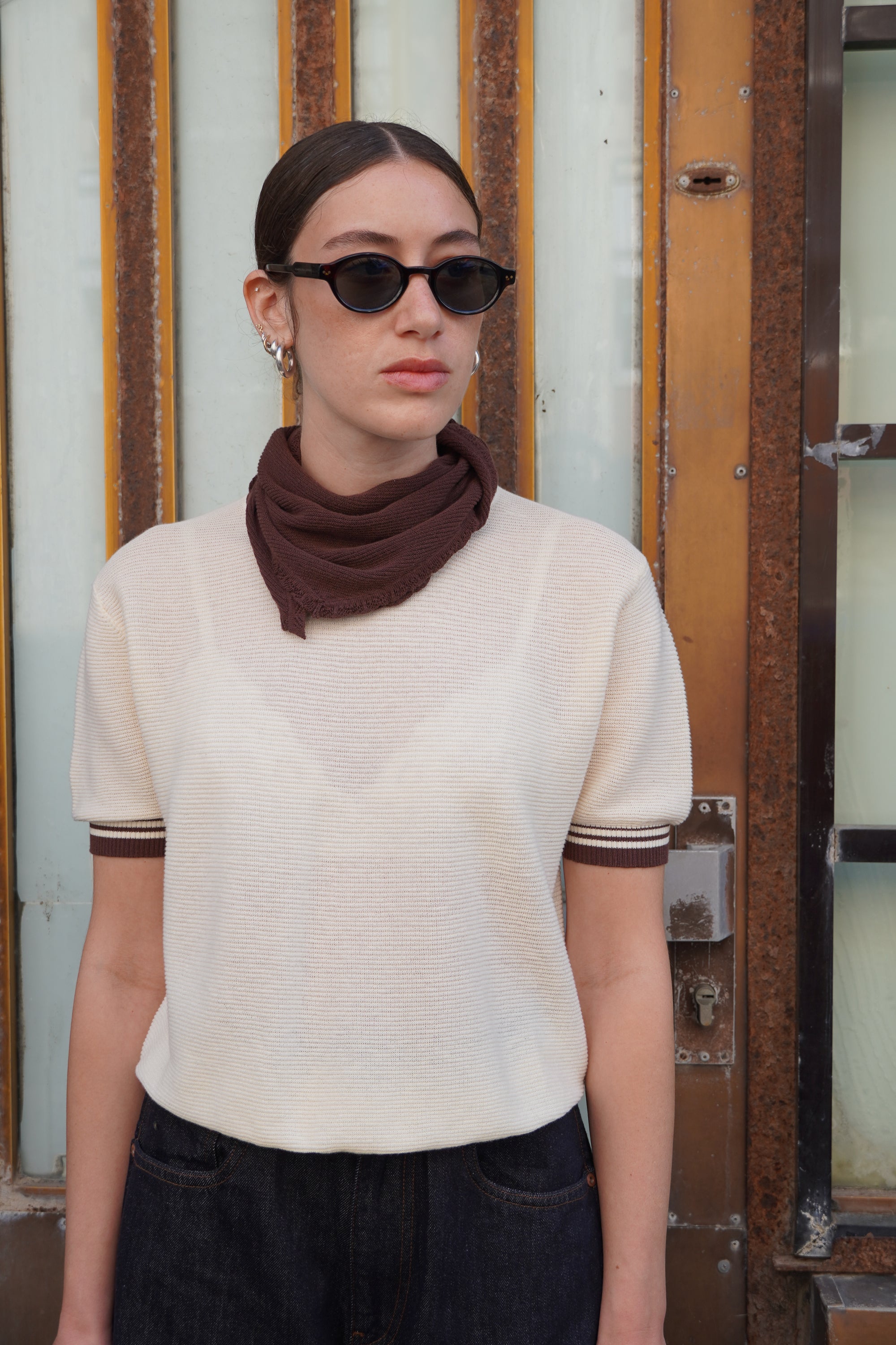 Model wearing a cream short-sleeve shirt with brown strips detail and a brown scarf.